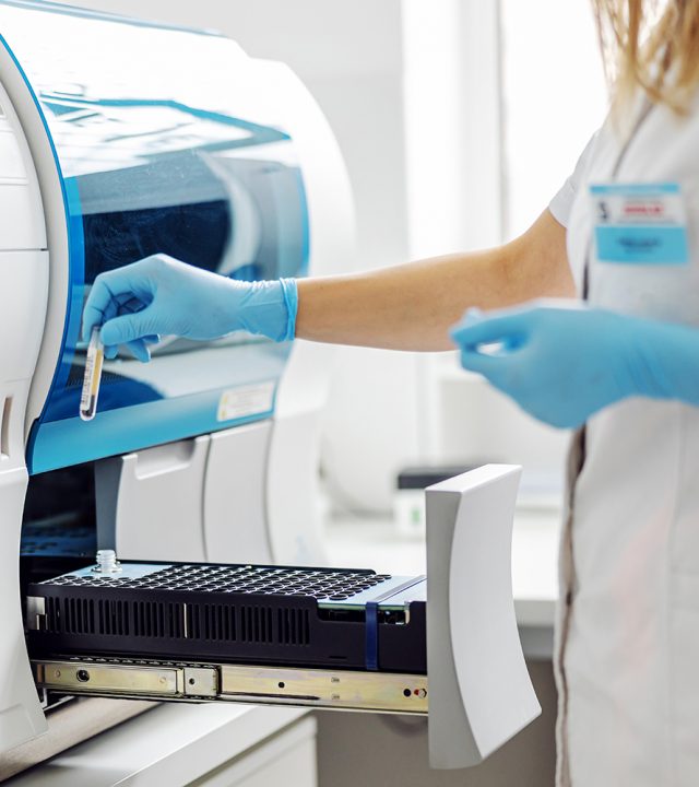 Female lab assistant putting test tubes with blood samples into machine.